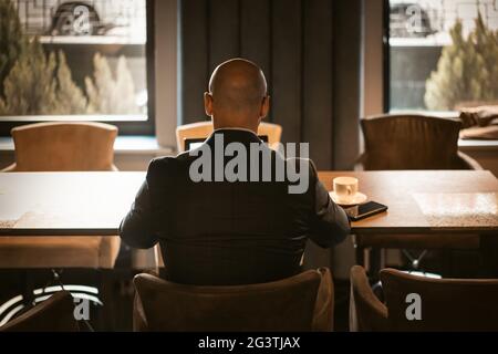 Vista posteriore di elegante amministratore delegato vestito in costume costoso seduto al tavolo nel moderno e costoso ufficio interni, cald maschile worki Foto Stock