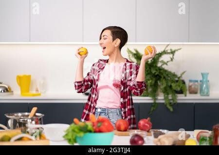 Madre felice con pomodori gialli freschi in mani che indossa camicia di plaid con una cottura corta di acconciatura nella cucina. Cibo sano Foto Stock