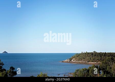 Vista dalla cima di una collina che si affaccia sul Mar dei Coralli su una costa rocciosa a bassa marea sotto un cielo blu chiaro Foto Stock