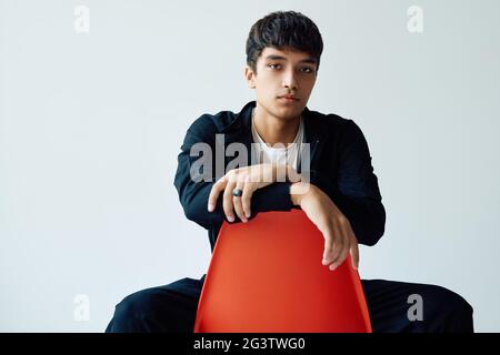 Elegante bel giovane uomo che posa in studio seduto su una sedia che guarda alla macchina fotografica Foto Stock