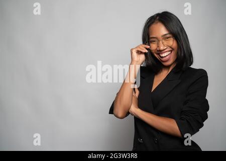 Attraente giovane donna asiatica in elegante blazer nero e vetri isolati su parete grigio chiaro Foto Stock