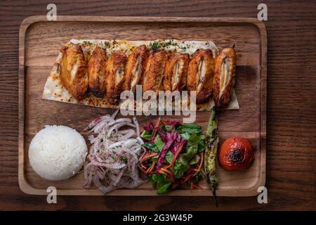 Ali di pollo turche o kebab di manzo con riso e verdure su tavolo di legno Foto Stock