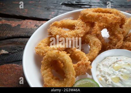 Anelli di calamari fritti con salsa a tuffo su tavolo rustico in legno Foto Stock