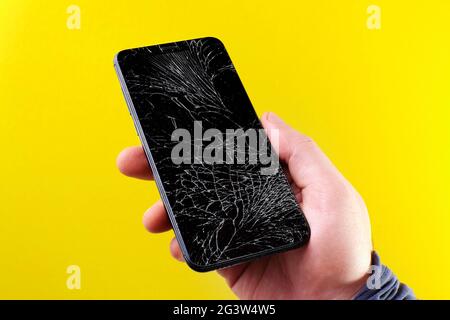 Smartphone nero con schermo a sfioramento rotto in mano su sfondo giallo. Foto Stock