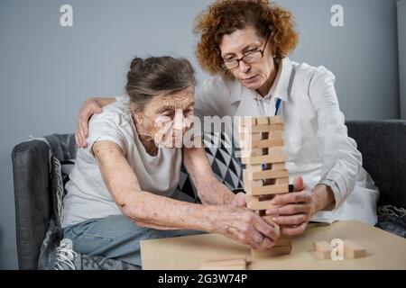 La terapia della demenza in modo giocoso, addestrando le dita e le abilità motorie fini, costruisce i blocchi di legno nella torre, giocando Jenga. Senior w Foto Stock