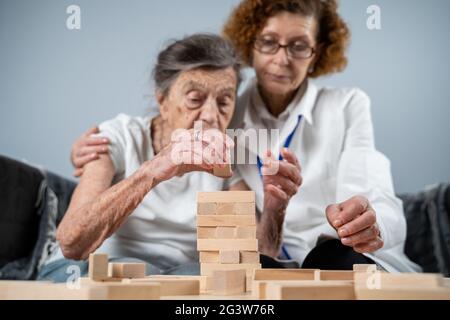 Jenga gioco. Il tema è la demenza, l'invecchiamento e i giochi per gli anziani. Caucasica anziana costruisce torre di blocchi di legno con il hel Foto Stock