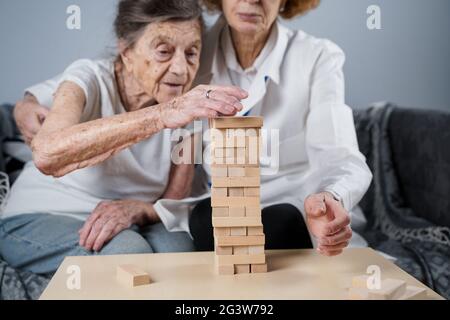 La terapia della demenza in modo giocoso, addestrando le dita e le abilità motorie fini, costruisce i blocchi di legno nella torre, giocando Jenga. Senior w Foto Stock