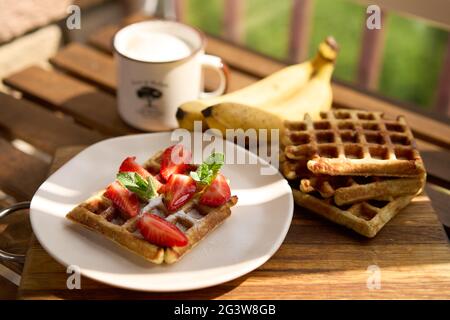 Vista della colazione, waffle belgi con fragola e banana con menta su sfondo di legno Foto Stock