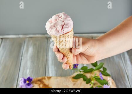 Cono per waffle con gelato su sfondo grigio con fiori. Foto Stock