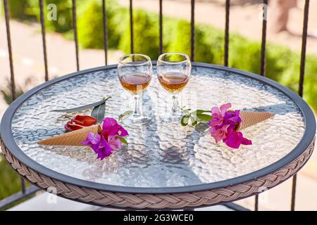 Aperitivo romantico a cena sul balcone. Cocktail estivi con fiori rosa di bougainvillea su un tavolo di vetro. Concetto di rinfresco. Estate fiori surreali luminosi e bevande fatte in casa. Spazio di copia. Alta Foto Stock