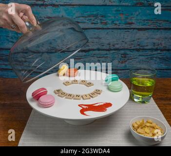Una mano femminile solleva un coperchio di vetro da un supporto per torta bianco che legge la buona mattina accanto a un bicchiere di succo e una ciotola di cereali Foto Stock
