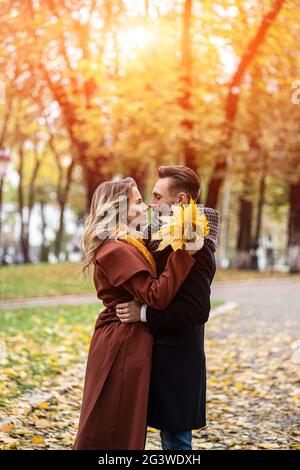 Marito e una moglie hanno abbracciato il sorriso guardarsi l'un l'altro nel parco autunnale. Ritratto di mezza lunghezza di una giovane coppia baciante. Outdoo Foto Stock