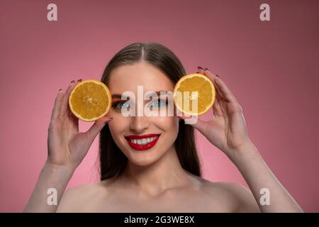 Ritratto di una giovane donna positiva con arance affettate in mani che si presentano affascinanti. Affascinante gioiosa signora divertente con capelli lunghi Foto Stock