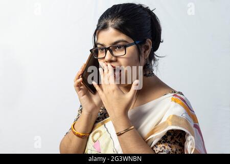 Una bella donna indiana in saree che parla di smartphone con viso sorpreso isolato su sfondo bianco Foto Stock