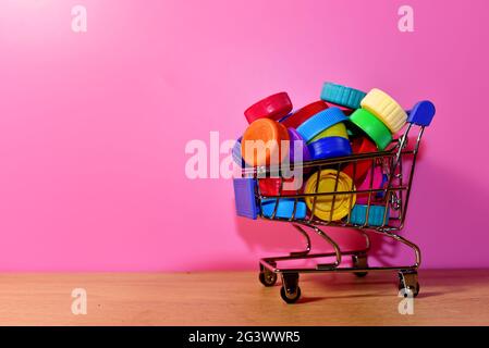 Tappi in plastica multicolore in carrello su sfondo rosa. Il materiale del tappo è riciclabile. Coperchi da bottiglie di plastica per riciclaggio Foto Stock