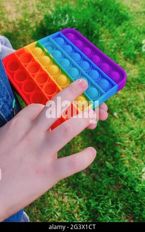 Un giocattolo rilassante alla moda che si schioccano nelle mani dei ragazzi. Un capretto sta tenendo il giocattolo del fidget di anti-stress popit. Gioco popolare per adulti e bambini. Foto di alta qualità Foto Stock