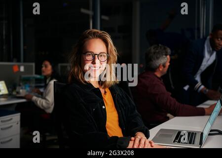 Ritratto di una donna esecutiva positiva in carica con colleghi che lavorano in background Foto Stock