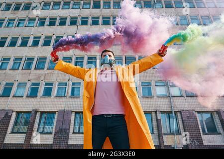 Giovane uomo in maschera respiratore tenere bombe di fumo in mani sollevate Foto Stock