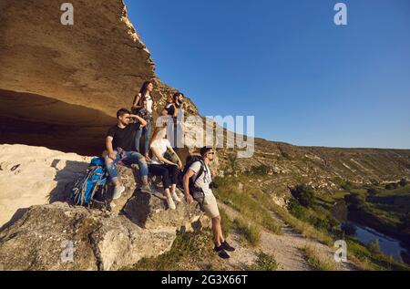 Gruppo di giovani turisti sorridenti escursionisti che si riposano su rocce naturali e godendo del verde paesaggio vallivo Foto Stock