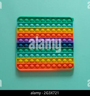 Giocattolo a righe in silicone brillante Big Pop IT primo piano su sfondo blu. Popit per bambini che giocano con l'arcobaleno, premendo le bolle con le dita, in alto Foto Stock