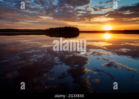 Scenico e bellissimo tramonto e suggestivo cielo nuvoloso e i loro riflessi su un lago calmo in Finlandia in estate. Foto Stock