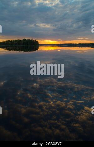 Scenico e bellissimo tramonto e suggestivo cielo nuvoloso e i loro riflessi su un lago calmo in Finlandia in estate. Foto Stock