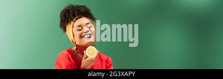 sorridente giovane afroamericana tenendo mezzo taglio di limone su verde, banner Foto Stock