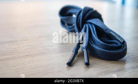 Un soggetto di lacci piatti blu scuro con punte sottili per le scarpe arrotolate e isolate su uno sfondo di legno. Accessorio elegante Foto Stock