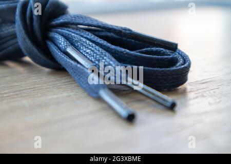 Un soggetto di lacci piatti blu scuro con punte sottili per le scarpe arrotolate e isolate su uno sfondo di legno. Accessorio elegante Foto Stock