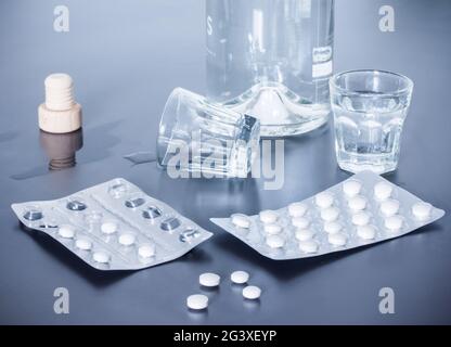 Abuso di droga: Primo piano di pillole e alcol su una tavola grigia Foto Stock