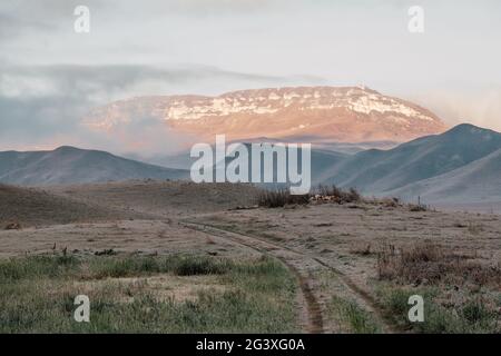 Strada sterrata in campo che va in montagna. Dawn nel campo autunnale. Colline nella foschia mattutina. Erba coperta di rombo autunnale Foto Stock