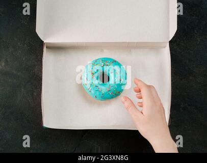 La mano raggiunge per ciambella in scatola di carta, vista dall'alto Foto Stock