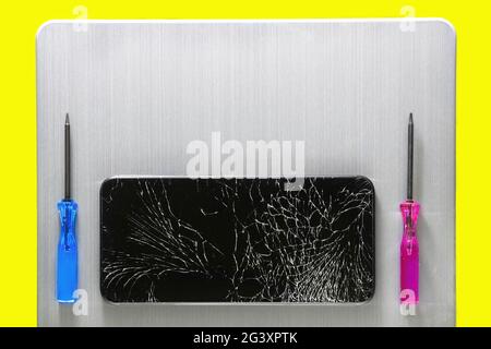 Un telefono touch con schermo rotto e cacciaviti si trovano su una superficie spazzolata in metallo grigio. Layout con spazio da copiare. Foto Stock
