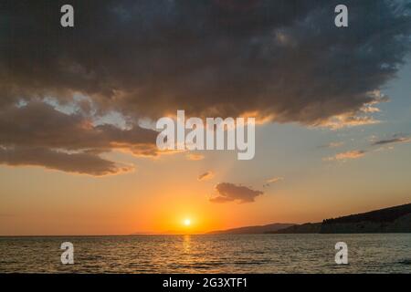 Il sole tramonta sull'orizzonte al mare, colore dorato del sole, calma al mare. Spesse nuvole colorate sulla superficie dell'acqua. Concetto - vacanza al mare Foto Stock