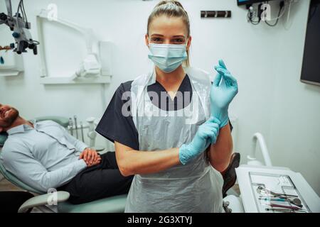 Infermiera caucasica che indossa guanti chirurgici in piedi in ufficio medico con cliente maschile Foto Stock