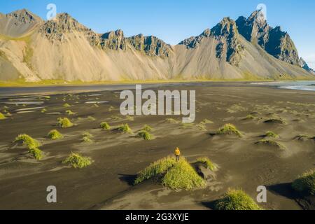 Islanda. Vista aerea dell'escursionista con zaino sulle dune di sabbia nera sul promontorio di Stokksnes, sulla costa sud-orientale islandese con Vestrahorn. Europa. Foto Stock