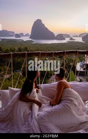 Coppia uomo e donna di mezza età in vacanza in Thailandia svegliarsi nella giungla con camera da letto all'aperto guardando l'alba sopra l'ocea Foto Stock