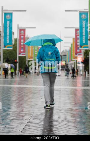 Wembley Stadium, Wembley Park, Regno Unito. 18 Giugno 2021. EURO 2020 ripara sotto un ombrello su Olympic Way, Wembley, mentre la pioggia torrenziale cade attraverso Londra. La Scozia affronterà l'Inghilterra nella seconda partita del Gruppo D del Campionato europeo di calcio UEFA allo stadio di Wembley questa sera con un calcio d'inizio alle 20:00. Credit: amanda Rose/Alamy Live News Foto Stock