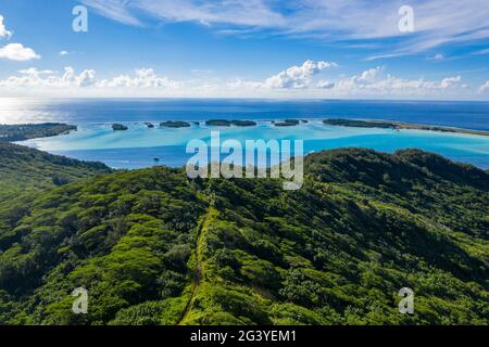 Vista aerea di quad ATV su strada sterrata attraverso la lussureggiante vegetazione di montagna con isolotti di Motu nella Laguna di Bora Bora in lontananza, Bora Bora, Leeward è Foto Stock