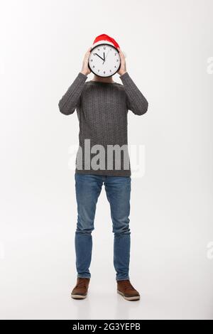 Concetto di vacanza - Giovane bello barba uomo nascosto dietro l'orologio bianco su bianco di sfondo per studio. Foto Stock