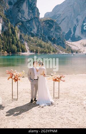 Lo sposo e lo sposo stanno in piedi per la cerimonia, con un arco di colonne di fiori d'autunno, sullo sfondo del Lago di Foto Stock