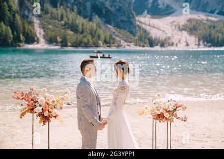 Lo sposo mette su un anello alla sposa, al luogo per la cerimonia, con un arco di colonne di fiori d'autunno, sullo sfondo di Foto Stock