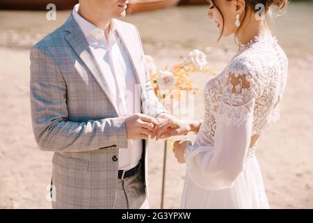 Lo sposo mette su un anello alla sposa, al luogo per la cerimonia, con un arco di colonne di fiori d'autunno, sullo sfondo di Foto Stock