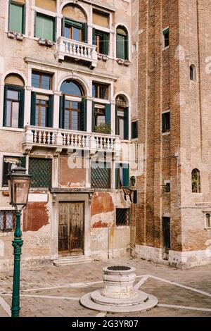 Primi piani di facciate di edifici a Venezia, Italia. Una vecchia strada ben nella piazza di fronte ad una casa di mattoni. Ci sono molti Venet Foto Stock