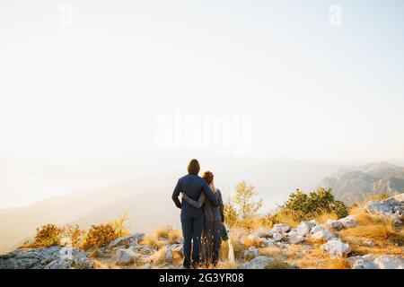 La sposa e lo sposo abbracciando il monte Lovcen alle loro spalle si apre una vista della baia di Cattaro, vista posteriore Foto Stock