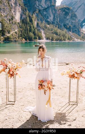 Bella sposa in un abito bianco con maniche e pizzo, con un bouquet giallo autunno sullo sfondo dell'arco per la cerimonia, a. Foto Stock