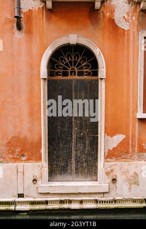Primi piani di facciate di edifici a Venezia, Italia. Una vecchia porta nera graffiata, in una porta ad arco, con una griglia forgiata arrugginita A. Foto Stock