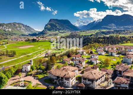 Vista aerea di improbabili prati verdi delle Alpi Italiane, Comano Terme, enormi nuvole su una valle, tetti di case, Dolomiti Foto Stock