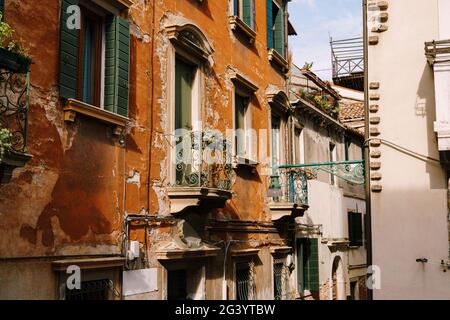 Primi piani di facciate di edifici a Venezia, Italia. Porta di legno verde in fondo alla casa di mattoni. Balcone con recinzione forgiata. Un vecchio Foto Stock
