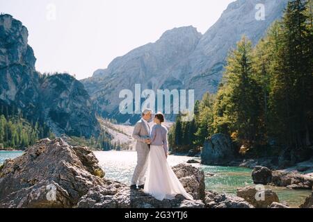 La sposa e lo sposo sono in piedi su pietre che si affacciano sul Lago di Braies in Italia. Matrimonio di destinazione in Europa, su Braies lak Foto Stock